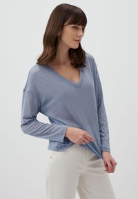 Lichtblauwe, lange mouwen V-hals top met een relaxte pasvorm, gemaakt van zachte, lichte stof, gecombineerd met witte broeken.
