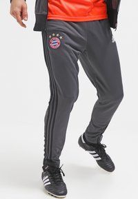 Grijze sportbroek met het logo van FC Bayern München, drie zwarte strepen aan de zijden, elastische tailleband en lichtgewicht materiaal.