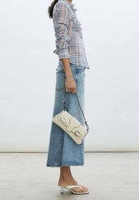 Bolso de cuero blanco con detalles de herrajes plateados, forma rectangular y correa desmontable, combinado con una camisa de cuadros azul y una falda de mezclilla clara.