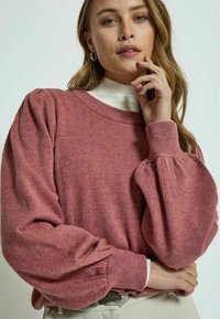 Light pink sweater with puffed sleeves and ribbed cuffs, made of soft textured fabric. Layered over a white turtleneck.