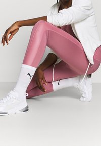 Leggings atléticos rosas con una textura suave, combinados con zapatillas deportivas blancas con acolchado, calcetines blancos con un logo negro y una chaqueta blanca con cremallera.
