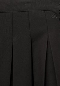 Nærbillede af sort plisseret stof med syet linning og små broderede initialer på højre side.