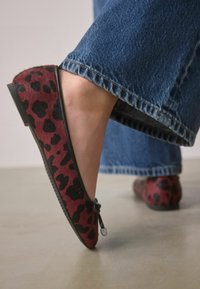 Burgundijas un melna leoparda raksta džinsu apavi ar mīkstu teksturētu virspusi un melnu zoli, ar dekoratīvu loku akcentu pie pirksta.
