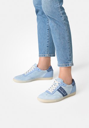 Blaue Wildleder-Sneaker mit einer Mischung aus hellen und dunklen blauen Paneelen, weißen Schnürsenkeln und einer strukturierten Sohle, kombiniert mit hellblauen Jeans.