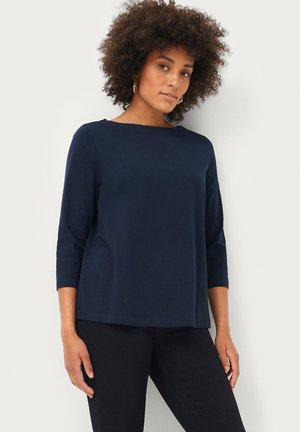 Haut bleu marine à manches 3/4 en tissu doux, avec un col rond et une coupe décontractée et ample, associé à un pantalon noir.