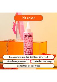 Une bouteille rose d'Amika Reset, étiquetée comme "huile de nettoyage du cuir chevelu au charbon rose", avec des motifs floraux et une pointe applicatrice pointue.