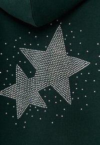 Groene hoodie met zilveren strassteentjes gerangschikt in twee grote stervormen, met kleinere strassteentjes verspreid rond het ontwerp.