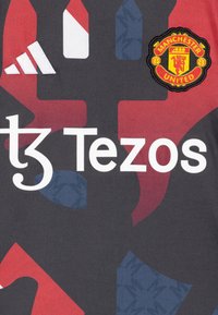 Dres Manchester United má tmavošedú základňu s červenými a modrými vzormi. Obsahuje prišité logo a biele textové označenie.