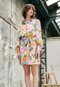 Blumenmusterkleid mit rosa, grünen und orangen Farbtönen, einem Kragen, langen Ärmeln und einem Bindegürtel in der Taille. Weicher Stoff.