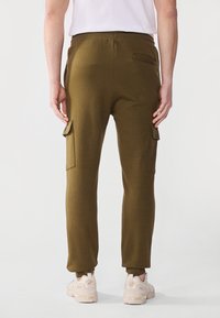 Olivgrüne Jogginghosen mit schmalem Schnitt, ausgestattet mit seitlichen Cargo-Taschen, elastischem Bund und gerippten Bündchen an den Knöcheln. Tragen Sie sie mit lässigen Sneakers.