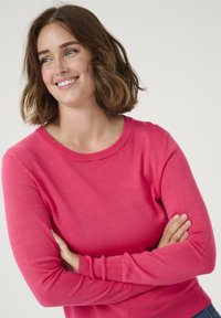 Pull en tricot rose avec un col rond et des manches longues, présentant une texture lisse et une coupe ajustée.