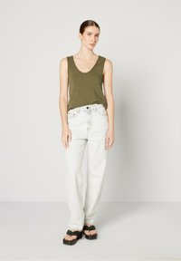 Green knitted tank top with a scoop neckline, paired with high-waisted light blue jeans and black platform sandals. Simple design and relaxed fit.