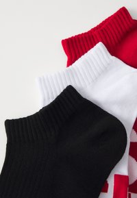 Tre paia di calzini alla caviglia: uno rosso, uno bianco e uno nero. Ognuno ha un bordo ribbed e una consistenza morbida, adatta per un abbigliamento informale.