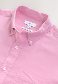 Vaahtopinkki nappipaita tavallisella istuvuudella, valkoisilla napeilla ja etutaskulla, asetettuna tasaisesti, kaulus osittain auki.