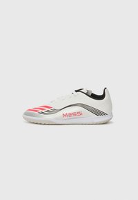 Witte zaalvoetbalschoenen met roze accenten, zwarte details en een gestructureerde bovenkant. Voorzien van strepen en 'MESSi'-branding aan de zijkant.
