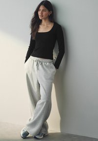 Zwart geribbelde langemouwen top gecombineerd met lichtgrijze sweatpants met een elastische tailleband en zijzakken; gedragen met grijze sportschoenen.