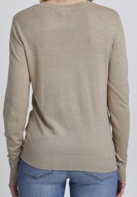 Hellbeige Pullover aus weichem Strickmaterial, mit langen Ärmeln und geripptem Saum, getragen mit blauen Jeans. Einfaches, klassisches Design.