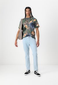 Blomstermønstret kortermet skjorte i grå og grønne toner, paret med lyseblå jeans og svarte sneakers, bærer en grå skulderveske.
