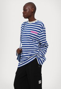 Μπλε και γκρι ριγέ μακρυμάνικη μπλούζα με ροζ γραφικό στο στήθος. Διαθέτει στρογγυλή λαιμόκοψη και χαλαρή εφαρμογή. Συνδυάζεται με μαύρο cargo παντελόνι.