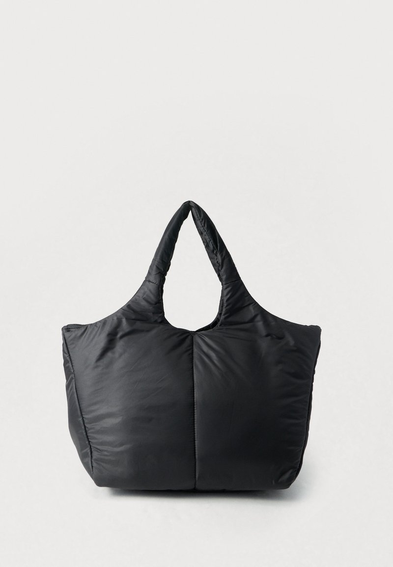 Grand sac fourre-tout noir matelassé avec des doubles poignées, une texture douce matelassée et une large base rectangulaire, debout sur un fond blanc.