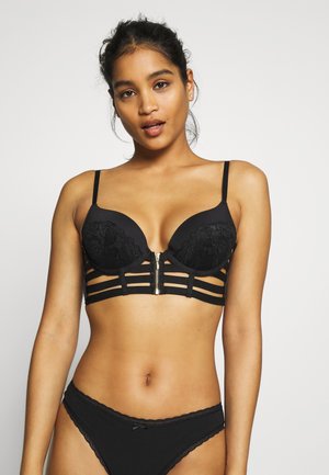 Reggiseno in pizzo nero con design strutturato, caratterizzato da cinturini verticali e una cerniera centrale. Le coppe lisce e i delicati dettagli in pizzo aggiungono eleganza.