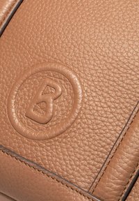 Brązowa skórzana faktura w zbliżeniu, z wytłoczonym okrągłym logo z literą "B" na środku, otoczona gładką lamówką.