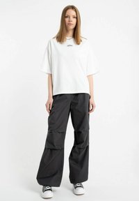 Biała oversize'owa koszulka z krótkim rękawem i małym logo. Czarne spodnie typu wide-leg o warstwowej konstrukcji. Czarno-białe sneakersy.