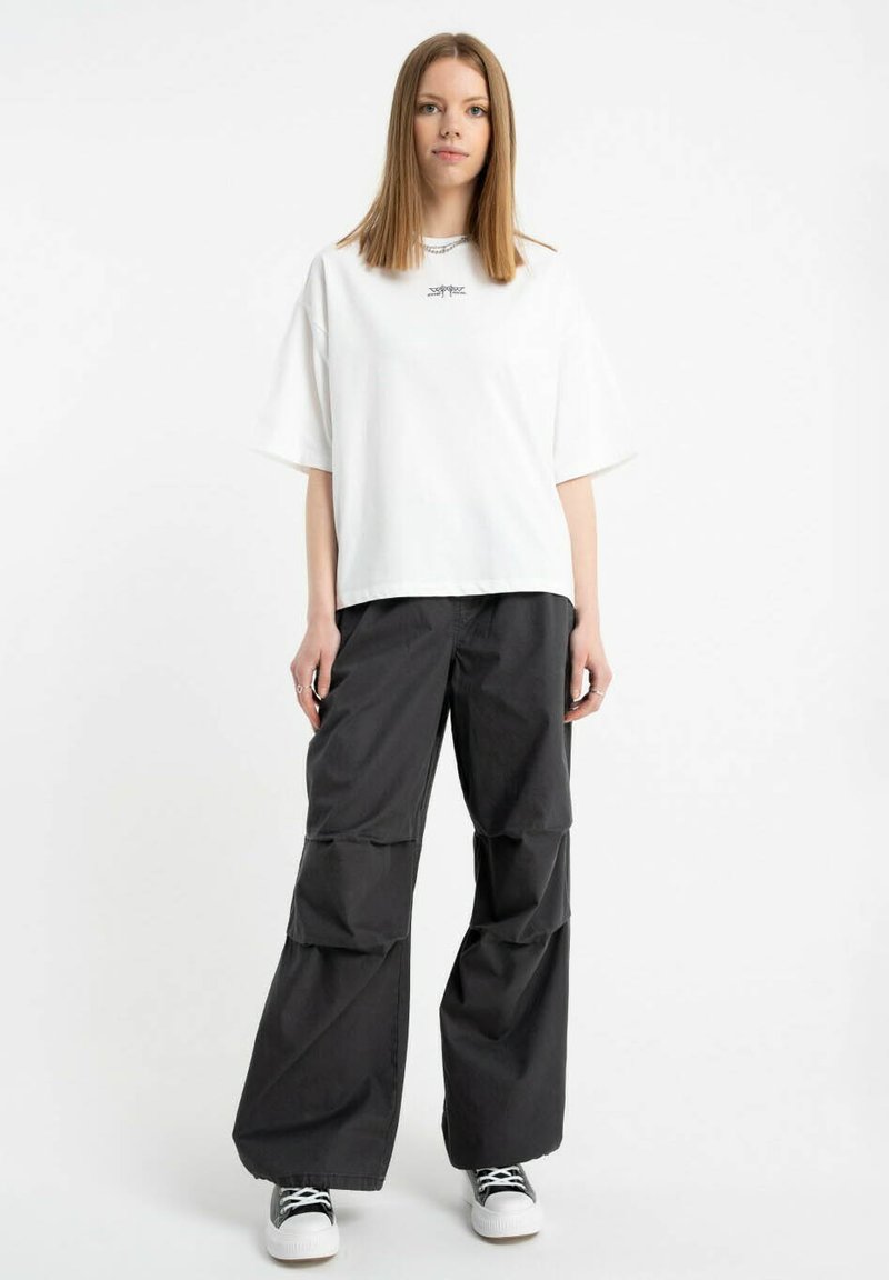 Biała oversize'owa koszulka z krótkim rękawem i małym logo. Czarne spodnie typu wide-leg o warstwowej konstrukcji. Czarno-białe sneakersy.