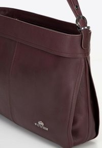 Sac à épaule en cuir bordeaux avec une texture lisse, marqué d'un logo argenté. Équipé d'une fermeture éclair et d'une sangle réglable.