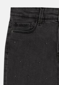 Jeans de mezclilla negros con un diseño clásico de cinco bolsillos y detalles metálicos dispersos en la parte delantera para agregar un toque adicional.