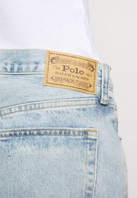 Light blue denim jeans with tan leather Polo Ralph Lauren label. Features includes visible stitching and a slightly distressed texture.