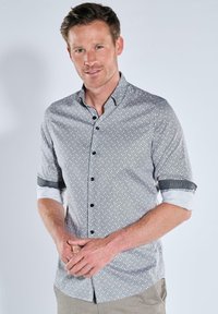 Herren Hemd mit Knopfleiste in einem schwarz-weißen geometrischen Muster, kurze Ärmel mit umgeschlagenen Manschetten, kontrastierende schwarze Akzente und einen strukturierten Kragen.