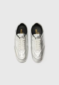 Sapatilhas metálicas prateadas com uma textura suave, apresentando uma biqueira arredondada, atacadores brancos e a marca "LOVE MOSCHINO" na língua.