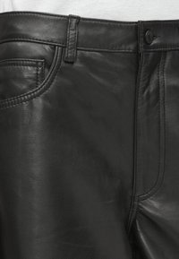 Zwarte leren broek met een gladde textuur, klassiek vijf-pocket ontwerp, zichtbare stiksels en een knoopsluiting bij de tailleband.