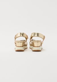 Auksiniai metaliniai sandalai su masyviu kulnu, reguliuojama kulkšnies juosta ir balta gumine outsole. Ypatybės: sklandi tekstūra ir minimalistiškas dizainas.