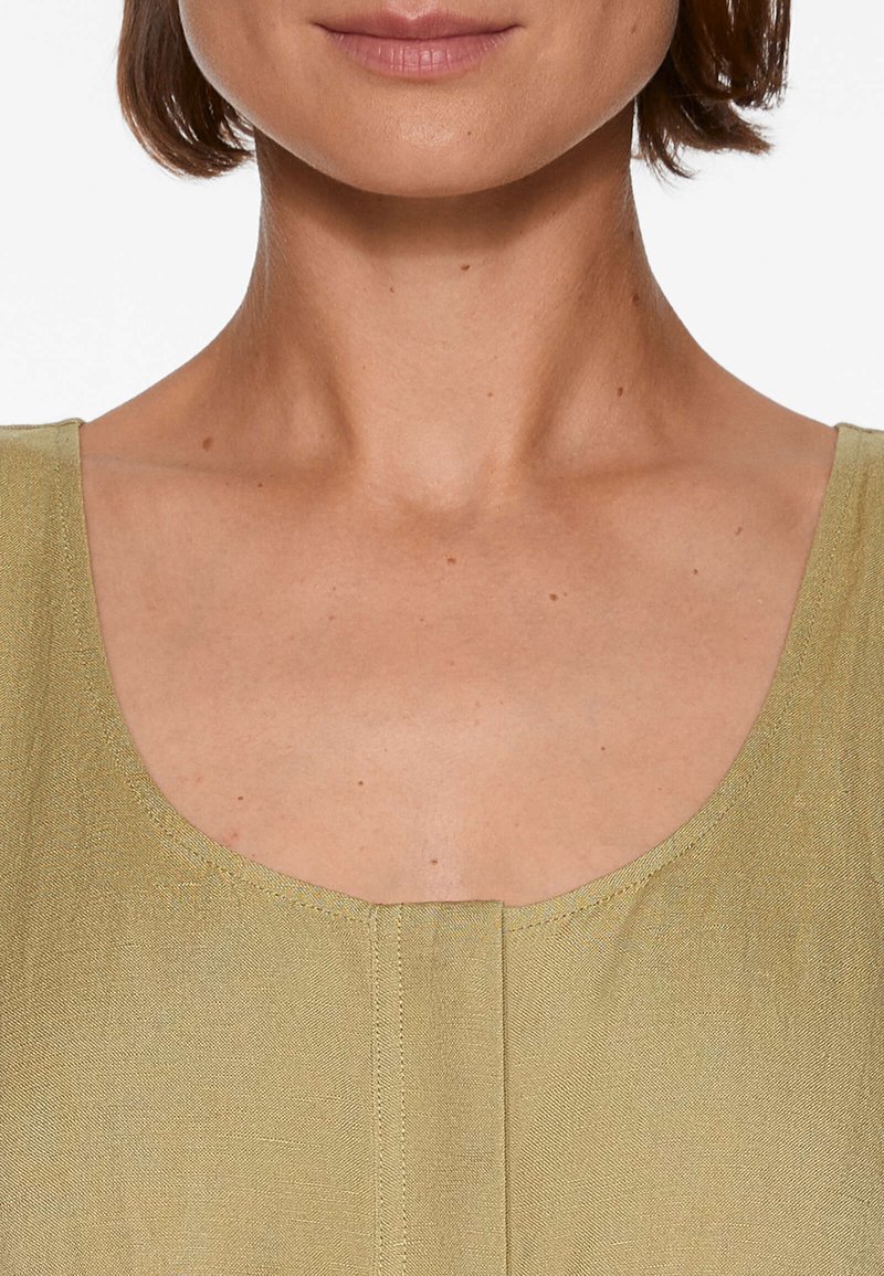 Olivgrünes enganliegendes Top mit weitem Rundhalsausschnitt, glatter Textur und zentraler Nahtdetail. Ärmelloses Design, minimale Nähte.