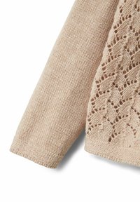 Stickad tröja i ljusbeige, med ett texturerat mönster på ena sidan och en slät finish på ärmen. Ribbad mudd avslutar designen.