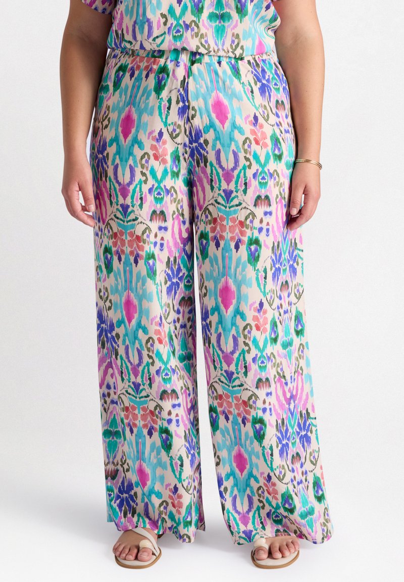 Des pantalons larges colorés présentent un motif mélangé vibrant avec des verts, des roses et des bleus sur un fond beige. Tissu léger et doux.
