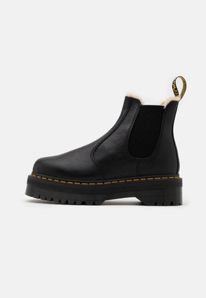Schwarzer Chelsea-Lederstiefel mit grober Sohle, gelber Naht, elastischem Seitenteil und sichtbar pelzgefüttertem Knöchelkragen.