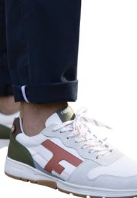 Baskets blanches avec des accents gris, vert et marron ; maille texturée et cuir lisse ; lacets ronds blancs avec un motif rouge ; logo sur le talon.