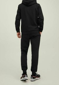 Set di felpa nera e pantaloni della tuta, realizzato in tessuto morbido. Presenta un orlo a coste, pantaloni con polsini e sneaker sportive nere e rosse.