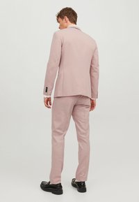 Pantalon rose clair au design ajusté, avec une fente simple et des accents de boutons noirs, associé à des chaussures noires. Texture de tissu lisse.