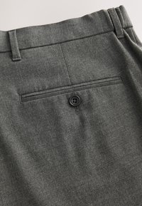 Poche arrière d'un pantalon gris foncé avec fermeture par bouton et passants de ceinture sur fond clair.