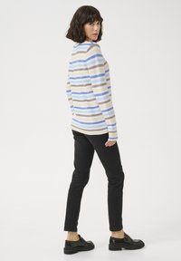 Gestreifter Strickpullover in Beige, Hellblau und Braun, kombiniert mit schwarzen Slim-Fit-Hosen und schwarzen Schuhen, von hinten betrachtet.