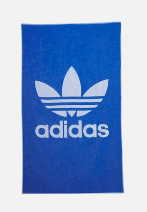 Asciugamano blu con logo bianco adidas. Presenta un grande design del trifoglio sopra il nome del marchio in lettere grasse e chiare, con una texture uniforme.