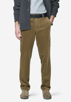 Man wearing brown corduroy pants, gray cardigan, white shirt, black woven belt, and brown suede shoes, standing with hands in pockets.