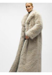 Lang, lysegrå faux fur frakke med bred krave og struktureret overflade. Frakken har en lige pasform og bæres åben med den ene hånd som holder kanten.