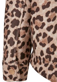 Close-up of leopard print jacket sleeve with brown and beige spots and a gold snap button on cuff.