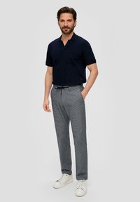 Polo azul marino con un bolsillo, combinado con pantalones de cuadros grises y zapatillas blancas. Diseño casual con mangas cortas y un ajuste cómodo.