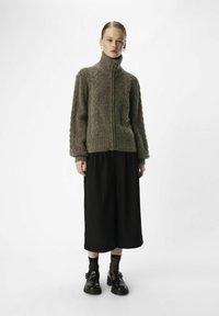 Suéter marrón de punto trenzado con cremallera y cuello alto, combinado con pantalones de pierna ancha negros y zapatos negros. Material liso y texturizado.